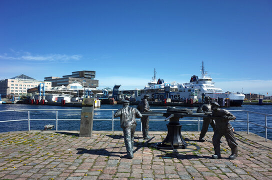 Helsingborg, Sweden - 04 May, 2018: Maritime sculpture of sailors working a capstan with Scandlines ferry terminal and Marina Plaza on background