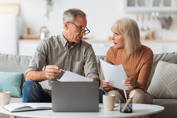 Senior Couple Holding Papers Reading Documents Sitting At Laptop Indoor