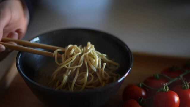 Closeup of woman girl eating the Chinese dish of noodles with tomatoes in a black bowl with chopsticks at a restaurant or at home.