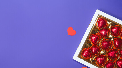 chocolates in a box, with red love heart shaped chocolate on violet background. Trendy Color of Year 2022 Very Peri.