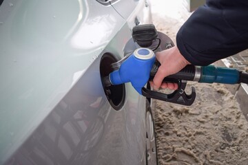 A man's hand directs a hose into the gas tank of a car at a gas station on a winter day