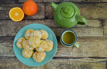 Homemade orange crinkle cookies with powdered sugar icing. Cracked citrus biscuits on wooden background. Served with tea