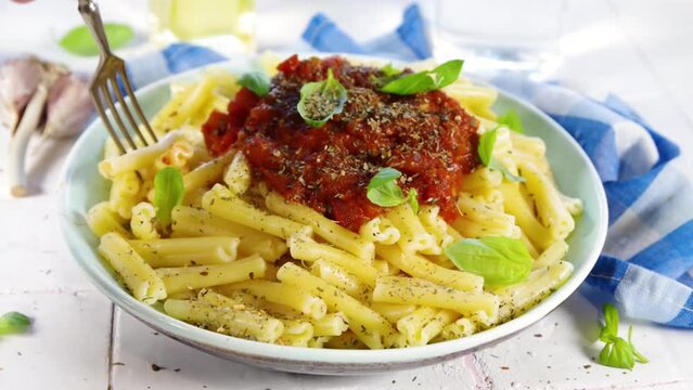Cooking Italian Casarecce pasta, with tomato marinara sauce, dried herbs and basil leaves, white tiles background