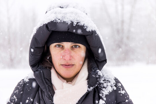 Tranquil female in warm outerwear covered with snow standing in forest in winter while enjoying stroll 
