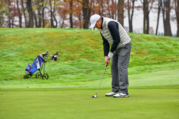 Fototapeta premium A golfer on the green evaluates the slopes and distance to the hole before aiming the ball towards the flag.