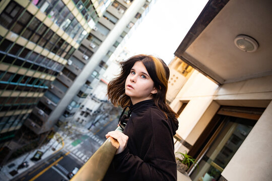 teen girl on the balcony of a city building looks at the city
