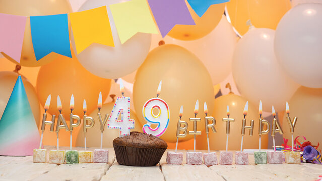 Happy birthday greetings for 49 years from gold letters of candles burning against the background of mine space balloons. Beautiful birthday card with muffins for forty-nine