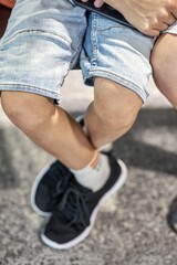 Obraz premium Legs of boy wearing denim shorts sitting on armchair and holding smartphone near brother in waiting room of airport extreme closeup