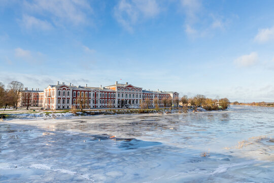 Baroque square residential building at the frozen river bank, ice reflecting the building seen from traffic bridge. Beautiful palace in the city of Jelgava at sunny winter day.
