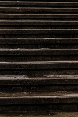 Vertical close-up photo of dark, wet, concrete steps at winter. Old weathered stairway texture for background. Pattern of vintage stone stairs. Set of steps at winter. Urban lines in city.  
