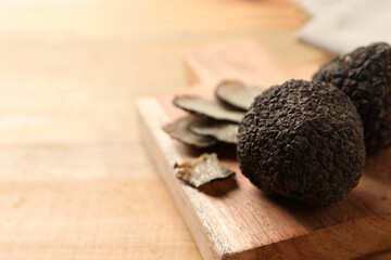 Black truffles with board on wooden table, closeup. space for text