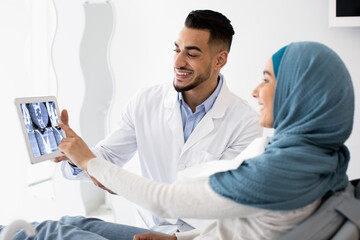 Obraz premium Orthodontist Doctor Showing Teeth Xray On Digital Tablet To Muslim Female Patient