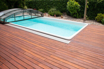 Outdoor swimming pool with cover enclosure and teak wood deck - obrazy, fototapety, plakaty