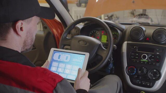 View from backseat of auto mechanic sitting in car and using diagnostic app on digital tablet