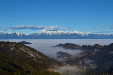 Fototapeta premium View of mountains Grintovec, Skuta and Kocna in Kamnik-Savinja alps in Slovenia with fog bellow the mountains and between the forest covered hills
