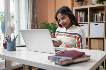 African American female student sitting at table attending online class at home 