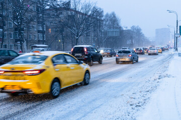 cars drive on snowy city road in blue winter dusk
