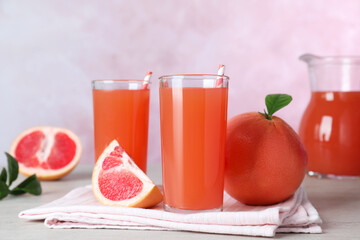 Tasty freshly made grapefruit juice and fruits on white wooden table