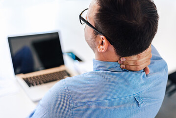 Businessman office working holding sore neck pain from desk working and sitting all day using laptop computer or notebook suffering neck ache sick worker overworking concept copy space closeup