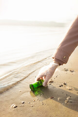 Volunteer pick up a glass bottle from a beach