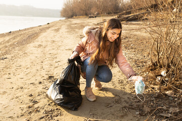A girl cleaning up the beach from various trash including face masks during the pandemic
