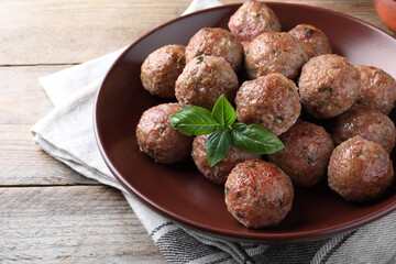 Tasty cooked meatballs with basil served on wooden table