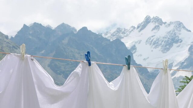 Drying fresh bed sheets on a clothesline against the mountains. Clean white linen dries outdoor among snowy peaks. 