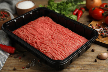 Minced meat in plastic container and other ingredients on wooden table