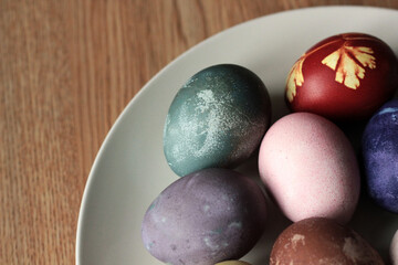 Easter eggs painted with natural paints in a plate on dish on wooden background. Top view point.