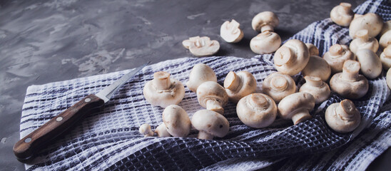 Fresh white mushrooms on a kitchen towel. Gray background. Knife next to champignons cut into slices. Kitchen, cooking, recipes. Mushrooms, ingredient. banner