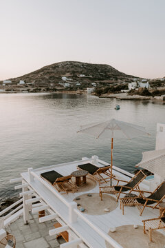 Relaxing scene at a holiday lounge deck by the sea overlooking blue waves and ocean, sun reflecting in water, blue sky and hills in the background
