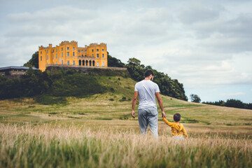 Dad and son walking through a meadow with a castle in the background. Man walking with his son....