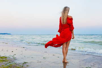 beautiful free woman in red dress in wind on sea beach