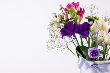 Different colors beautiful flowers bouquet in vintage white vase with ribbon on white background. Close up image with copy space.