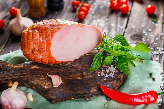 Meat balyk or boiled pork, whole or sliced on a kitchen cutting board, spices and cheese, vegetables, dark and moody, clouseup on a black wooden isolated background, top