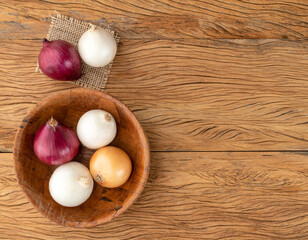 Assorted onions in a bowl over wooden table with copy space