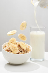 Oat porridge with levitating banana`s slices, walnut`s crumbs and glass of milk on a white background.