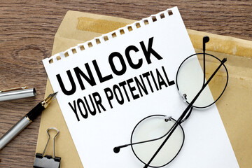Fototapeta premium unlock your potential - text on white paper from a notepad on a wooden background. glasses envelope and other supplies