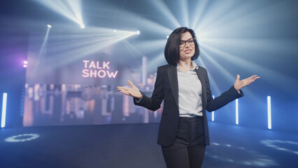 Happy presenter in a suit and glasses running onto the stage and announcing the start of the famous comedy, late-night show in an illuminated room with LED screen and 3D inscription