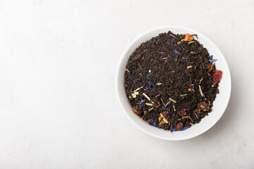 Dried fragrant black tea leaves in a bowl on a light cement background. Composition with organic, natural black tea. Top view. Copy space.