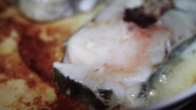 two pieces of Atlantic cod fish are fried in a white frying pan in fried carcass oil