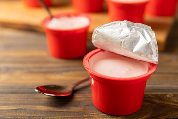 strawberry yogurt in a red plastic cup with a spoon on a dark wooden background.