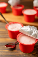 strawberry yogurt in a red plastic cup with a spoon on a dark wooden background.