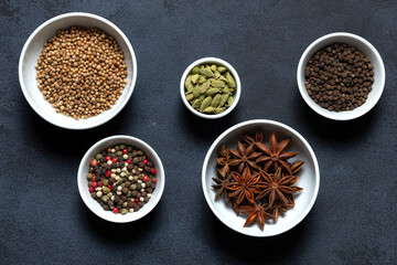 Spices assorted multicolor peppercorns, cardamom, star anise, cumin, coriander, caraway in bowls on black background.
