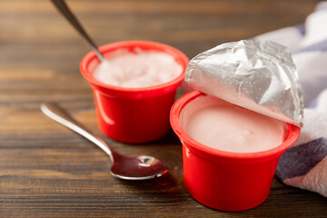 strawberry yogurt in a red plastic cup with a spoon on a dark wooden background.