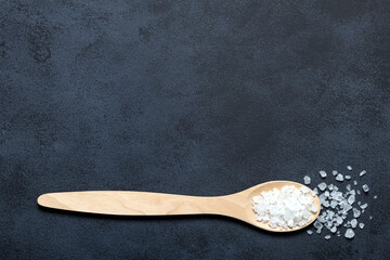 Salt in wooden spoon on black background copy cpace. Border.