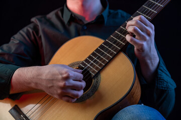 Obraz premium The guy in the dark shirt is plucking the strings of a six-string guitar