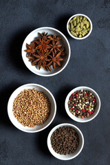 Spices assorted multicolor peppercorns, cardamom, star anise, cumin, coriander, caraway in bowls on black background.