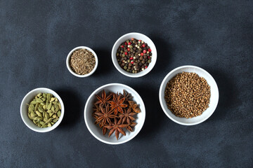 Spices assorted multicolor peppercorns, cardamom, star anise, cumin, coriander, caraway in bowls on black background.