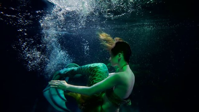 mysterious naiad is swimming in water of magical lake, art suit with fish tail for actress or model